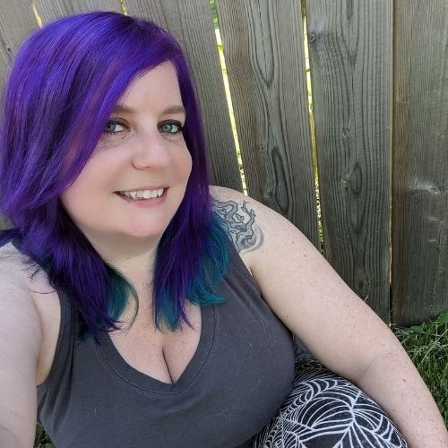 woman with purple hair sitting against wooden fence